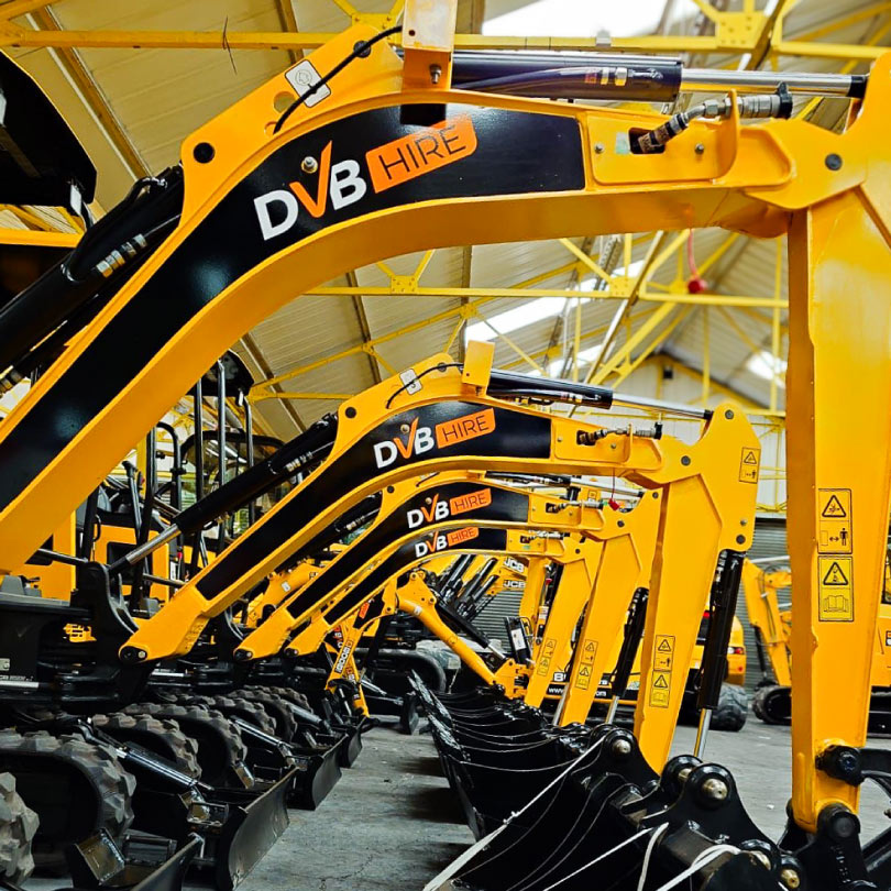 The image shows a row of JCB diggers. The arms have black vinyl wrap on the flat area with DVB Hire logos in orange and white.