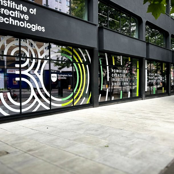 The image shows some street level windows. There is a printed and CAD Cut vinyl number 30 on across the whole window. The 30 consists of a series of offset strokes to create a modern style in white with some bold green accents. The logo for Nottingham Trent University is in the moddle of the zero.