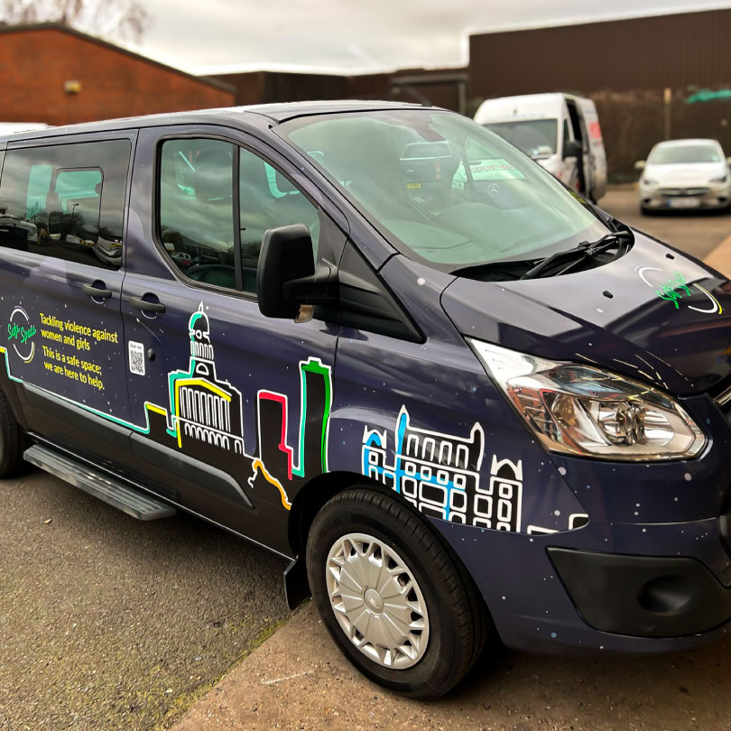 The image shows a full van wrap for NCC & Nottinghamshire Police & Crime Commissioner. The full wrap features Nottingham City Skyline illustrated with black silhouettes overlaid with white line drawings to add details to the building and bold colourful sectioning on the edges. This is on top of a subtle night sky gradient with small dots all over to represent stars. There is a safe space logo over the top with some type explaining what safe space does.